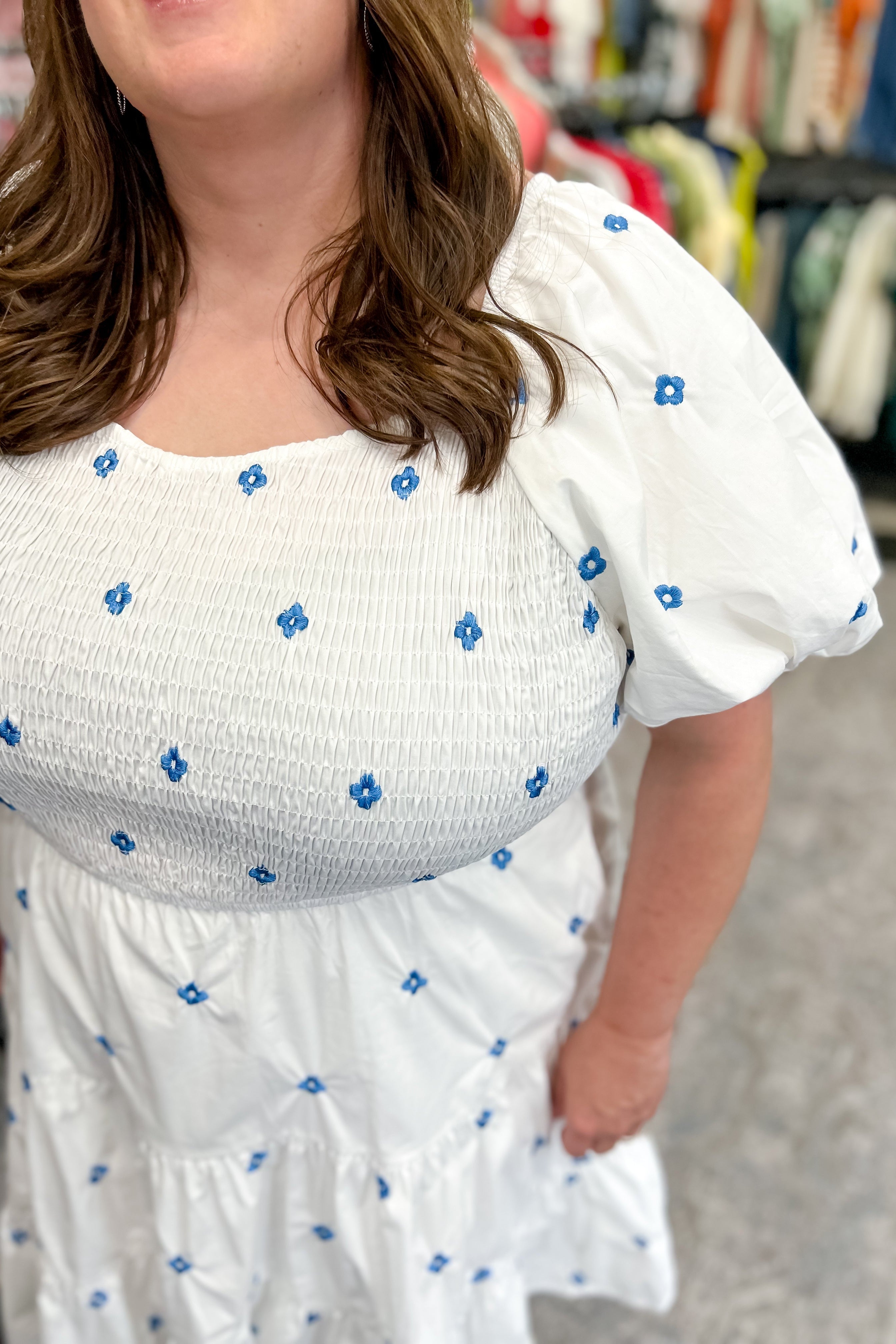 White dress with flowy bottom and smocked top. Round neckline. Short sleeve style. Blue floral embroidered detail. Hits right below the knee.