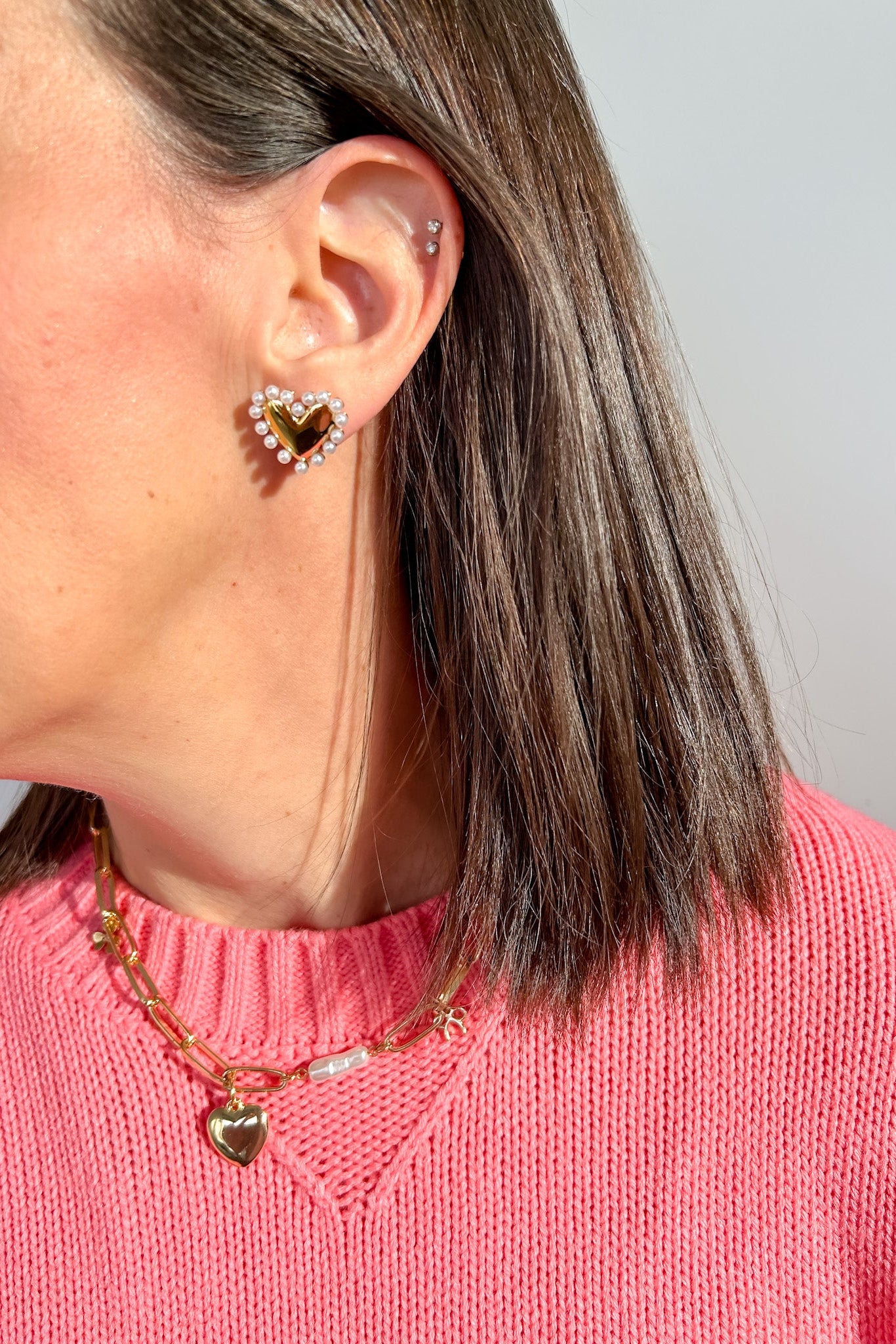 Person wearing heart-shaped earrings and a pink sweater with a necklace.