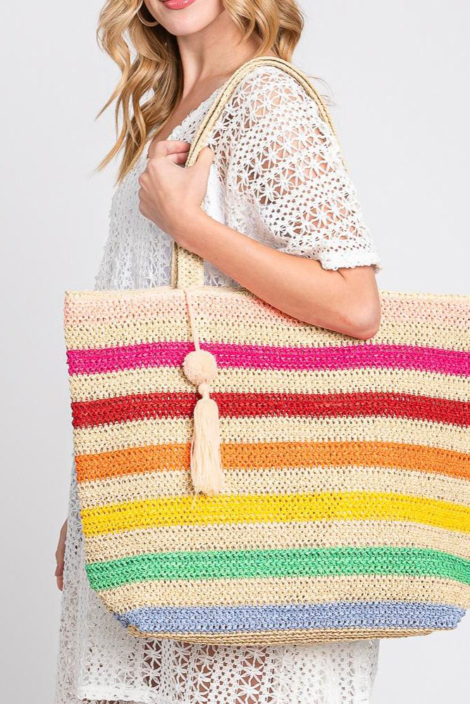 Photo of a model carrying a straw, crochet, striped tote bag with tassle