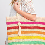 Photo of a model carrying a straw, crochet, striped tote bag with tassle