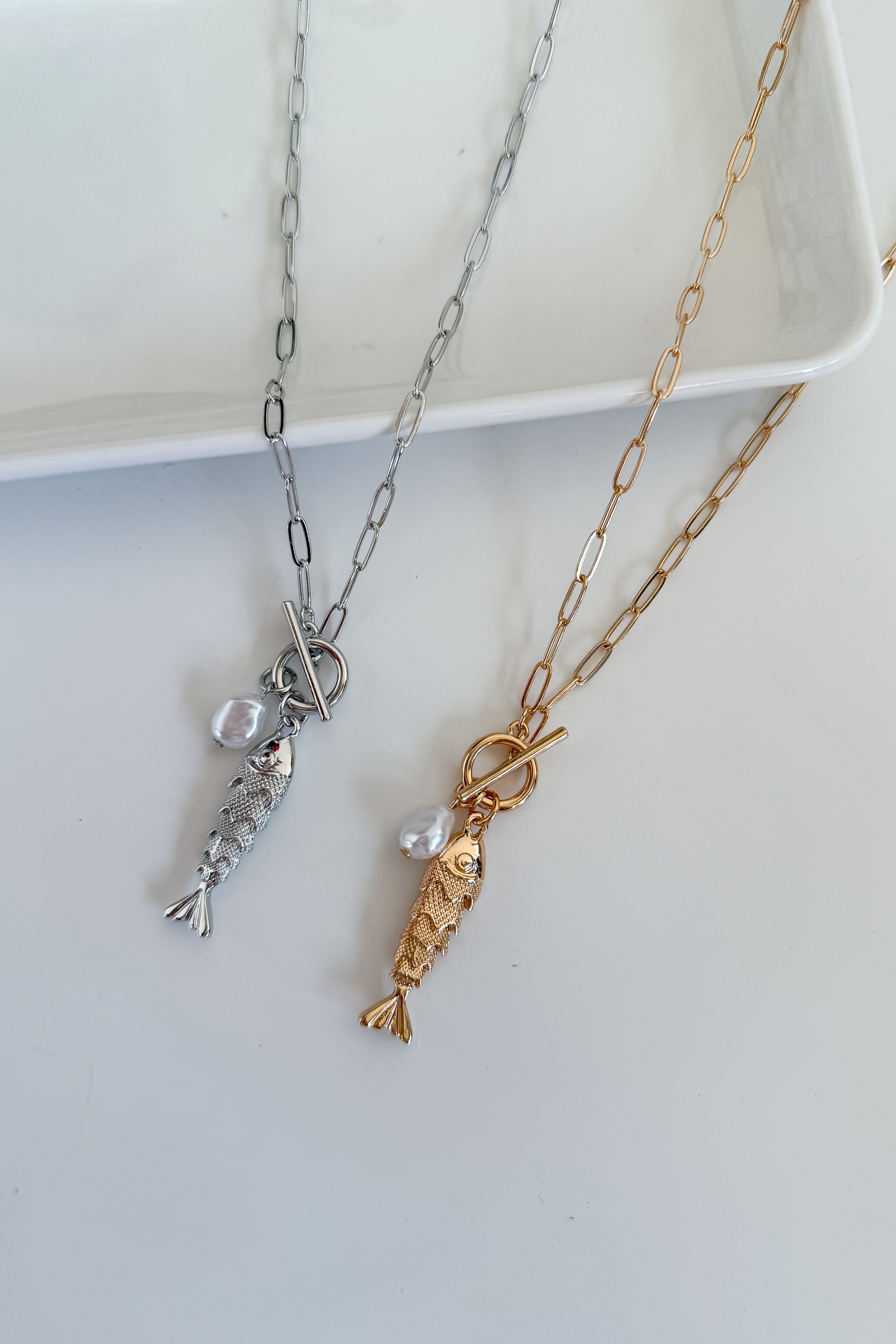 Two gold and silver fish-shaped pendants on chains against a white background