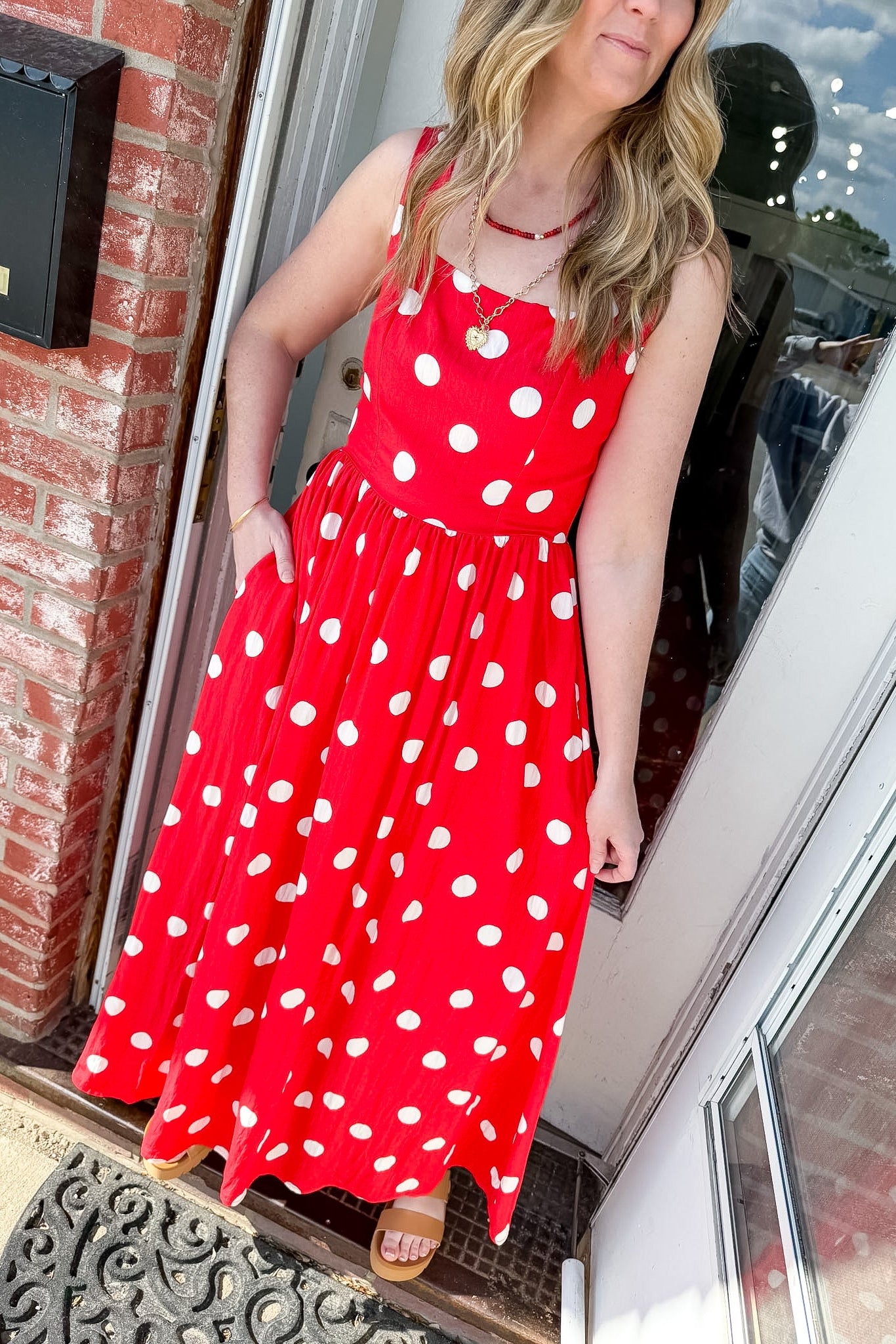 Woman wearing a red polka dot dress standing in front of a door.