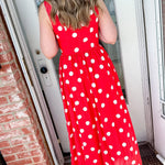 Person wearing a red polka dot dress standing in front of a door.