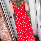 Person wearing a red polka dot dress standing in front of a door.