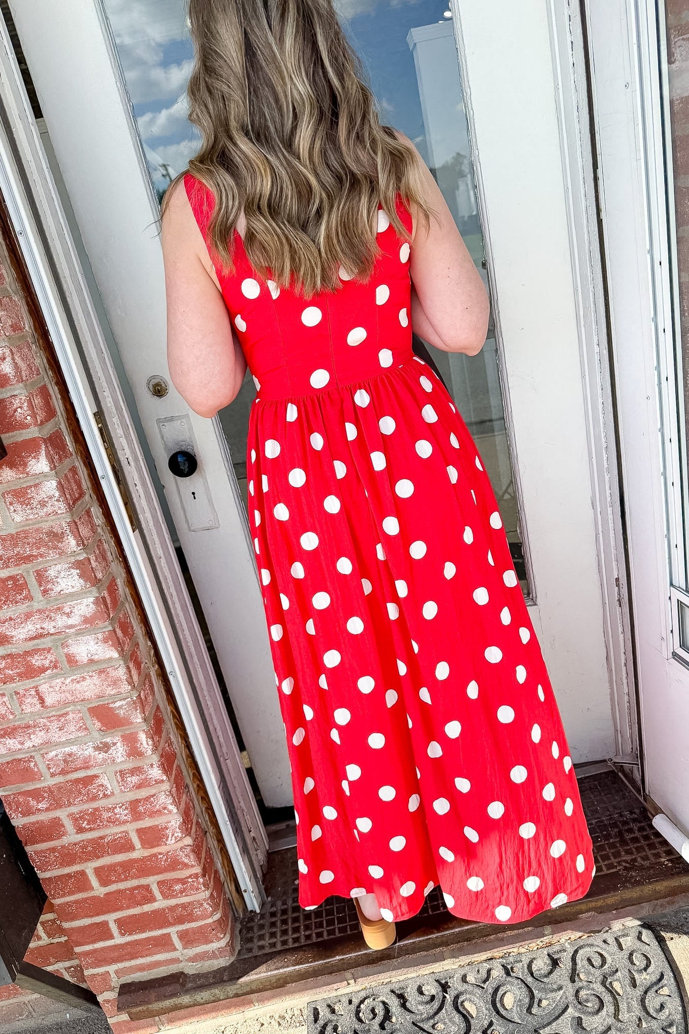 Person wearing a red polka dot dress standing in front of a door.