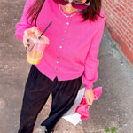Woman in a pink cardigan and black pants holding a drink on a sidewalk.