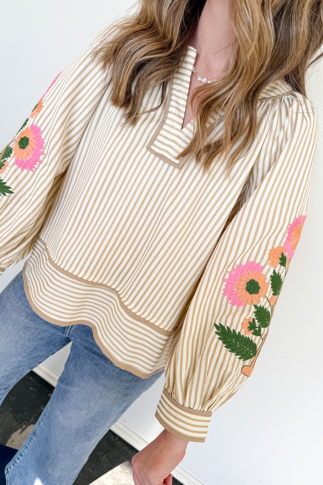 Woman wearing a beige striped sweater with floral embroidery on sleeves against a white background