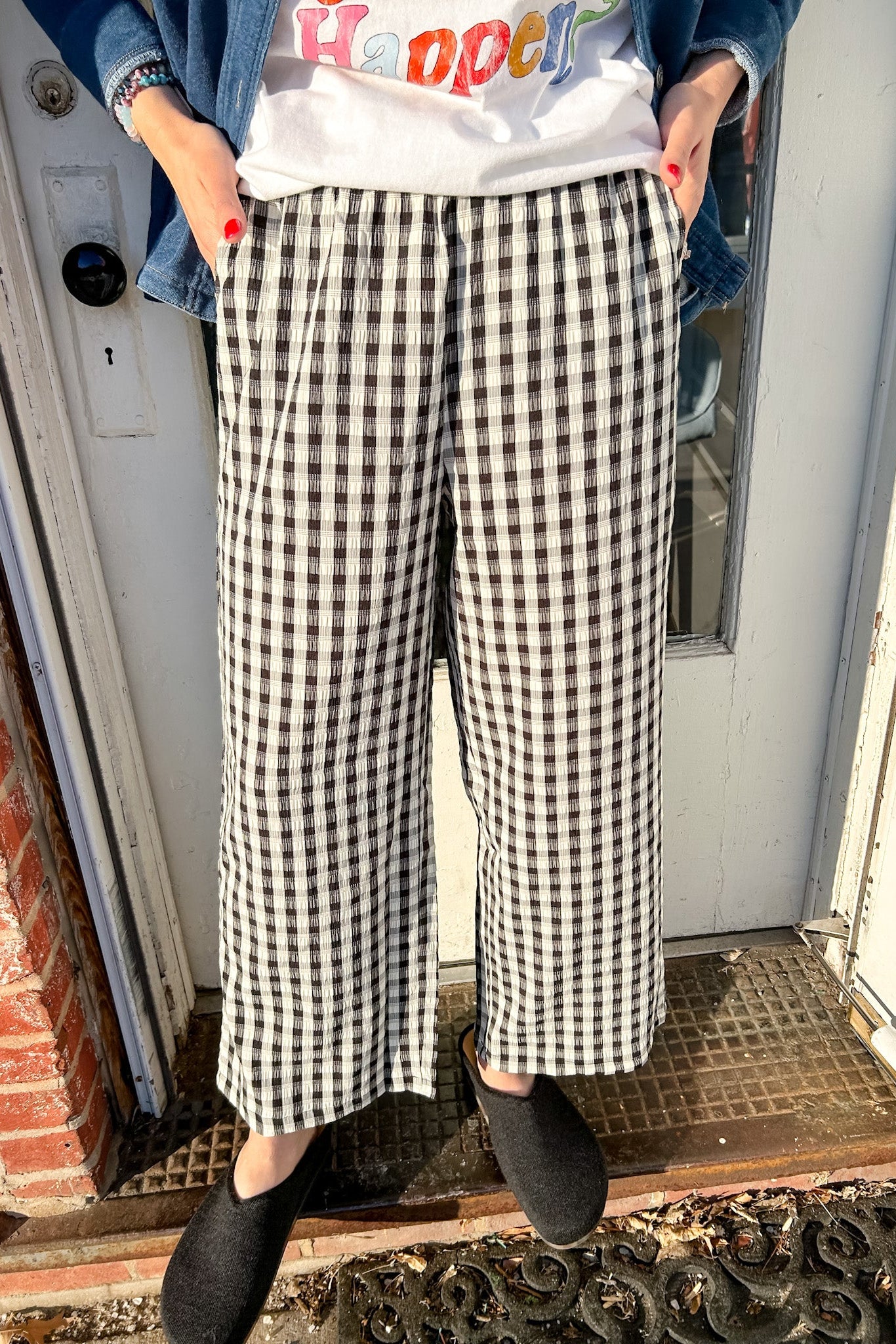 Person wearing a white shirt with colorful text, blue jacket, and black and white checkered pants standing on a doormat.