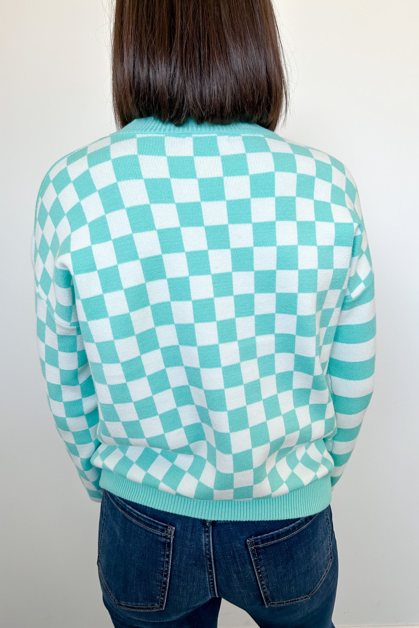 Person wearing a green and white checkered sweater against a plain background