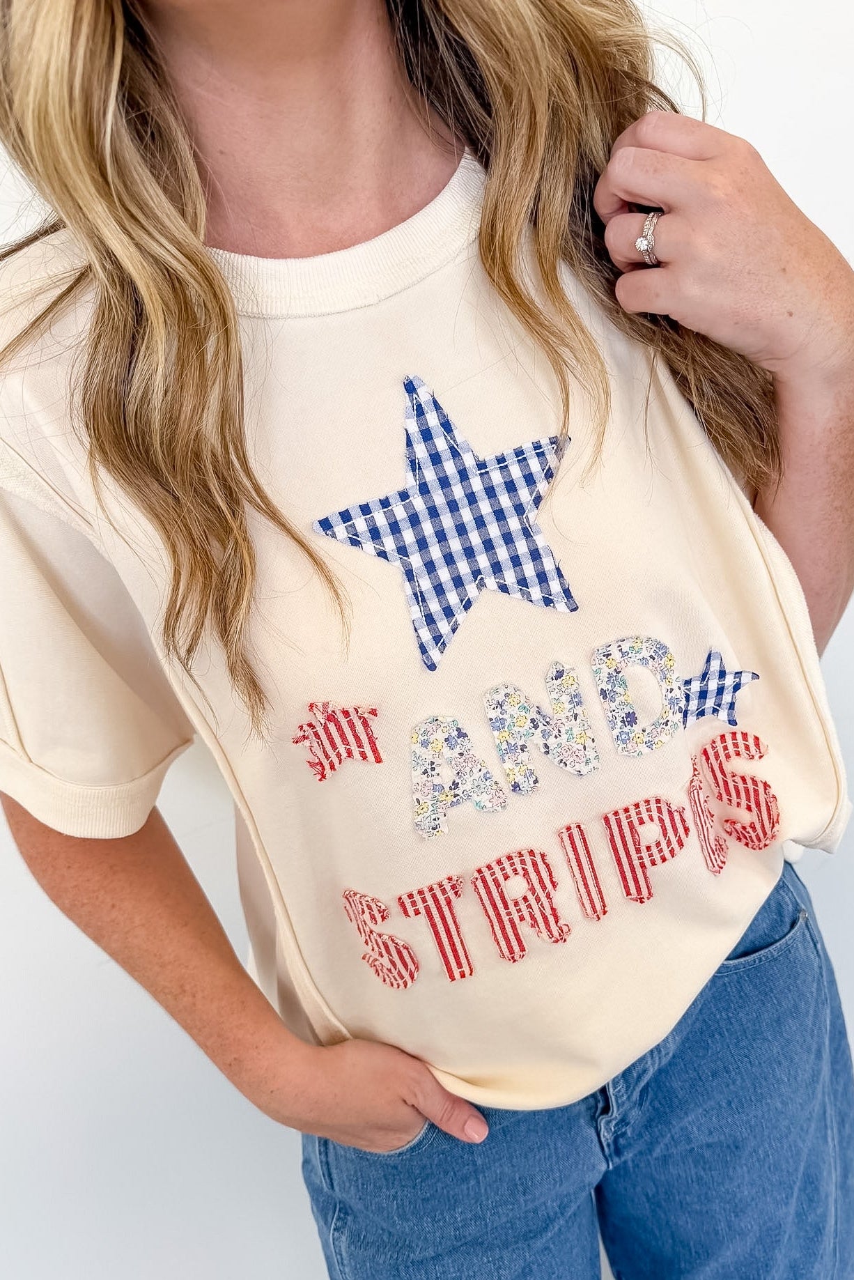 Person wearing a cream-colored t-shirt with a star and text design, standing against a white background.