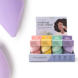 Two purple makeup sponges with a box of additional sponges on a white background