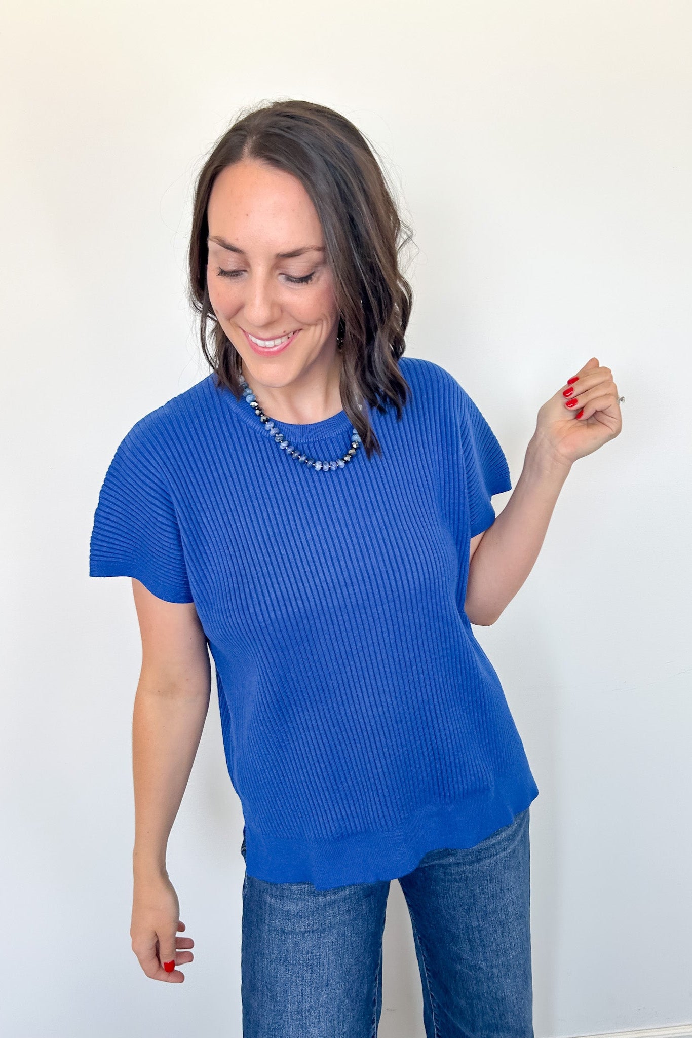 Woman wearing a blue ribbed sweater and jeans against a white background