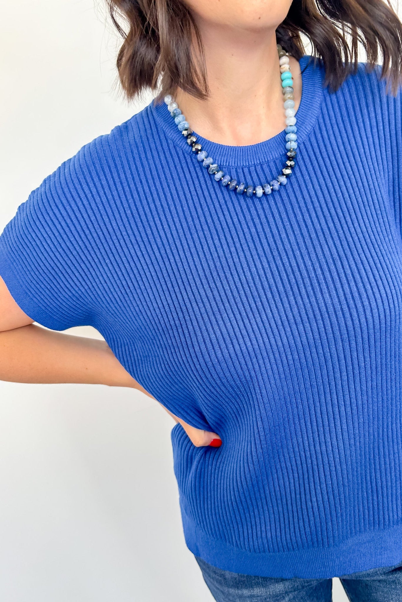 Person wearing a blue ribbed sweater with a plain background