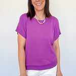 Woman wearing a purple shirt and white shorts against a plain background
