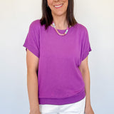 Woman wearing a purple shirt and white shorts against a plain background