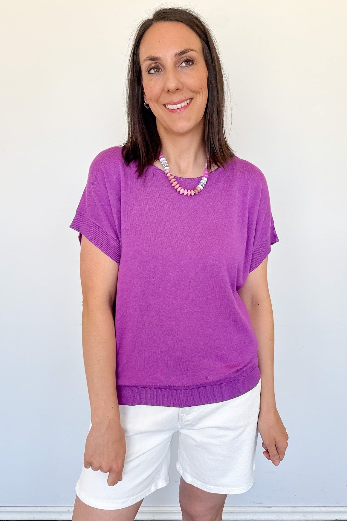 Woman wearing a purple shirt and white shorts against a plain background