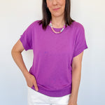 Woman wearing a purple shirt and white shorts against a light blue wall