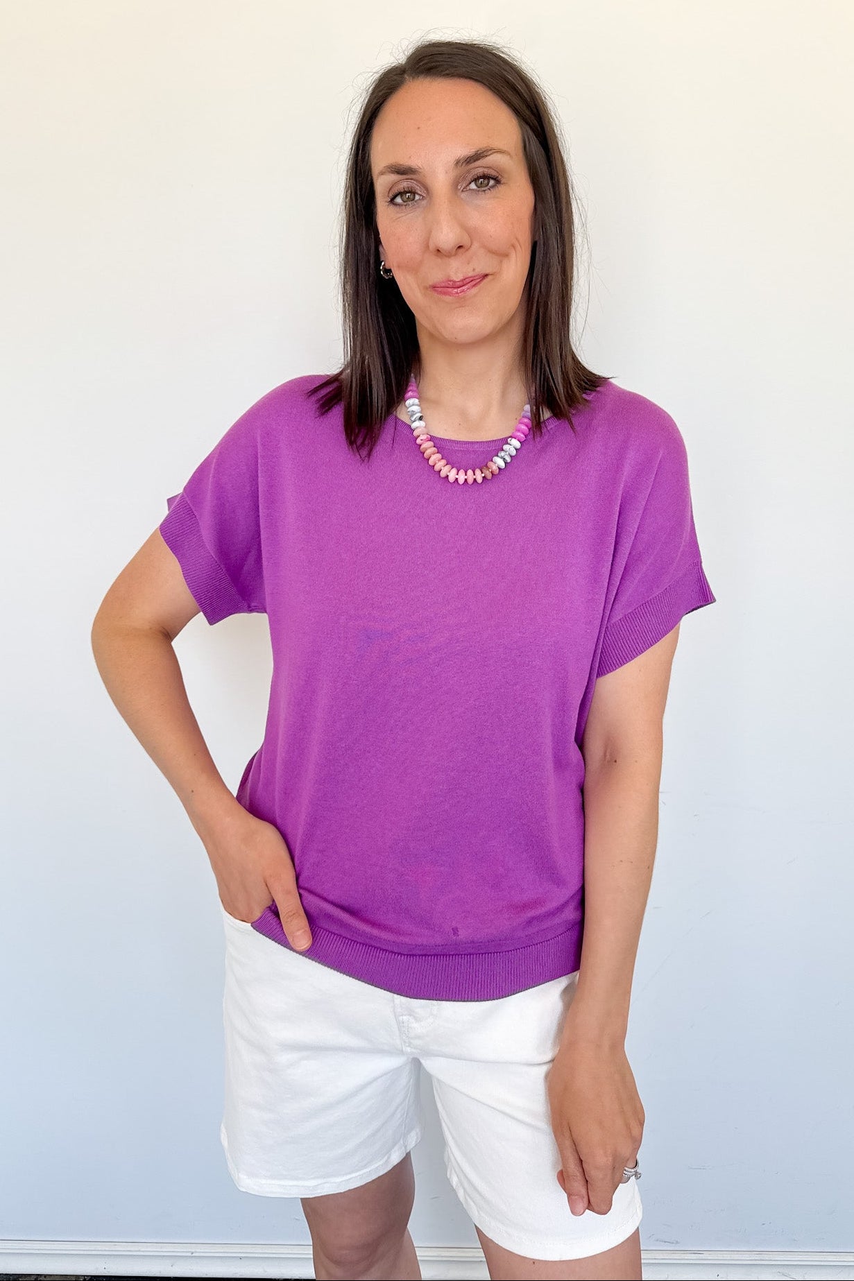 Woman wearing a purple shirt and white shorts against a light blue wall