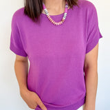 Woman wearing a purple shirt and white shorts against a light background