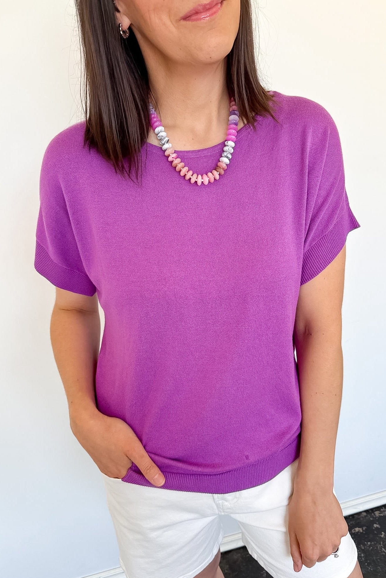 Woman wearing a purple shirt and white shorts against a light background