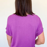 Person wearing a purple shirt and white shorts against a plain background