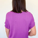 Person wearing a purple shirt and white shorts against a plain background