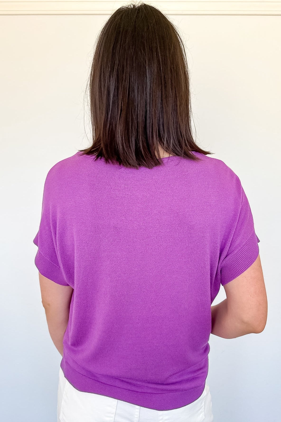 Person wearing a purple shirt and white shorts against a plain background