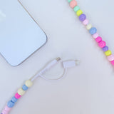 Colorful beaded phone charger on a light surface with a phone in the background