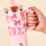 Pink tumbler with bow pattern held by a hand against a beige background