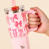 Pink tumbler with bow pattern held by a hand against a beige background