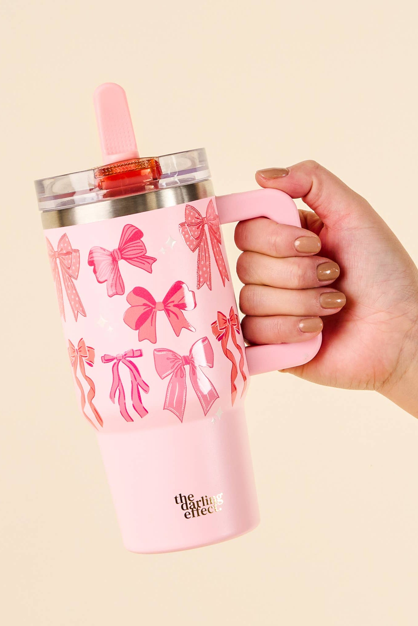 Pink tumbler with bow pattern held by a hand against a beige background