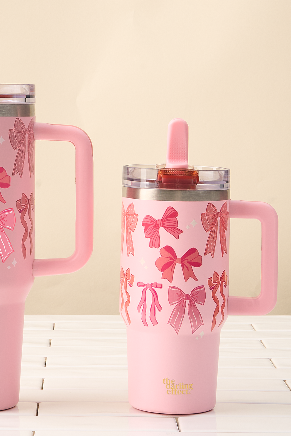 Two pink tumblers with bow patterns on a light wooden surface and beige background