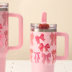 Two pink tumblers with bow patterns on a light wooden surface and beige background