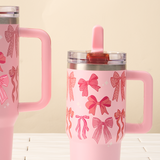 Two pink tumblers with bow patterns on a light wooden surface and beige background
