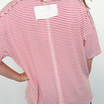 Person wearing a red and white striped shirt with a white label on the back against a plain background