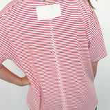 Person wearing a red and white striped shirt with a white label on the back against a plain background