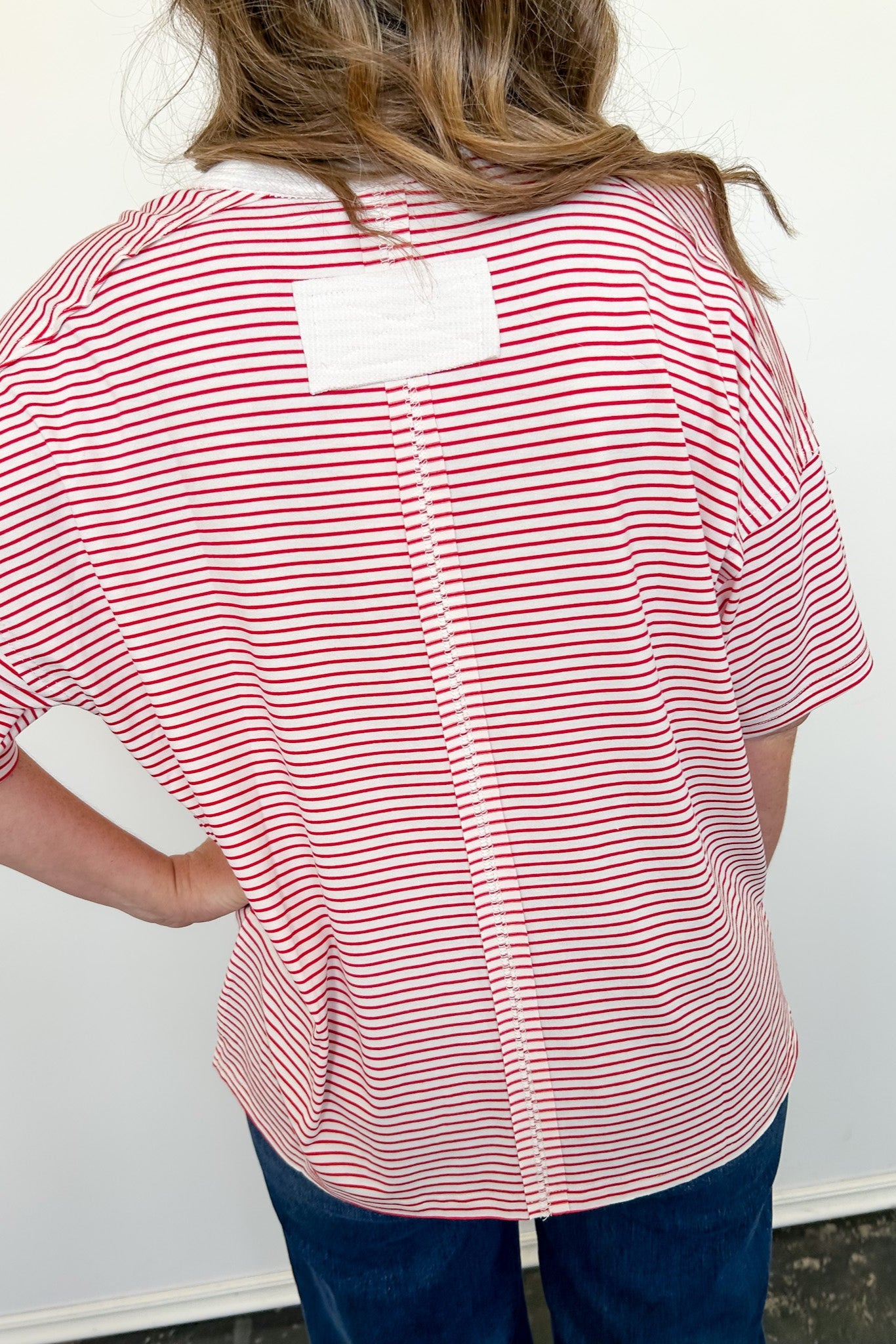 Person wearing a red and white striped shirt with a white label on the back against a plain background