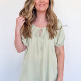 Woman wearing a light green striped blouse and blue jeans against a white background