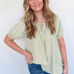 Woman wearing a light green blouse with short sleeves and blue jeans against a white background