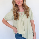 Woman wearing a light green blouse with short sleeves and blue jeans against a white background