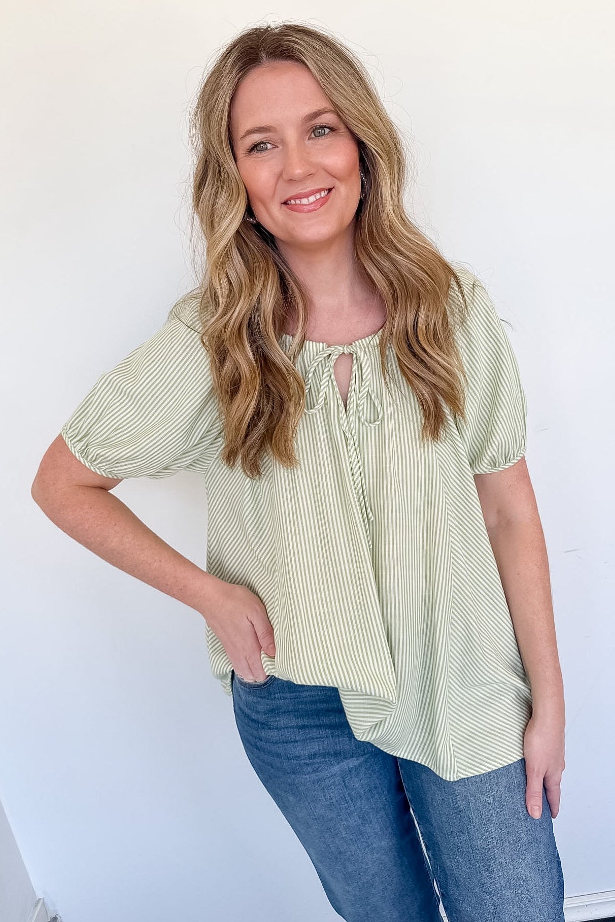 Woman wearing a light green blouse with short sleeves and blue jeans against a white background