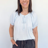 Woman in a light blue striped top that is short sleeve with charcoal grey shorts.