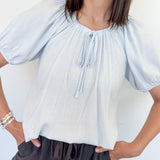 Woman wearing a light blue striped blouse and dark shorts against a white background