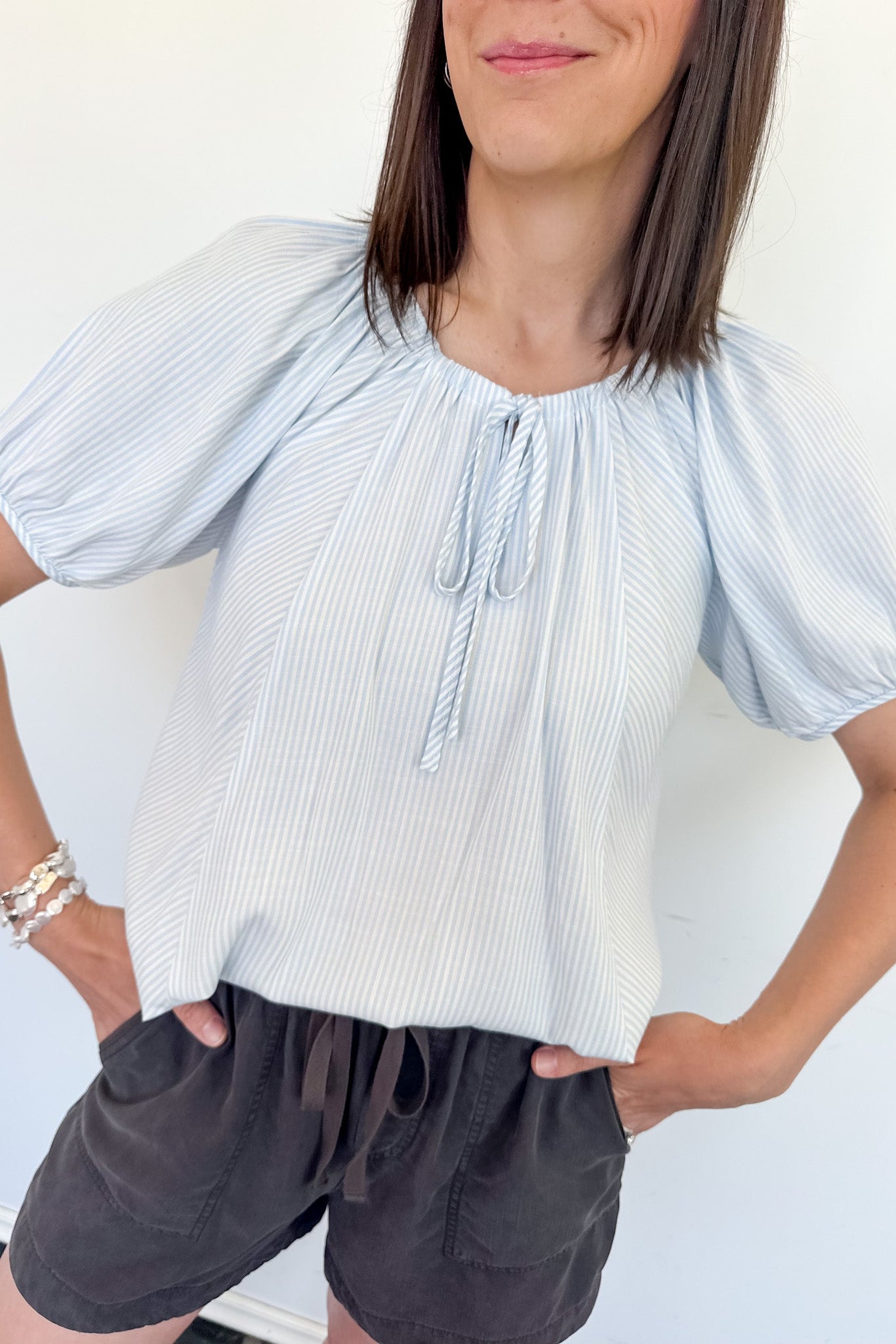 Woman wearing a light blue striped blouse and dark shorts against a white background