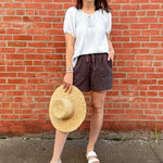 Woman standing in front of a brick wall with a light blue striped top on and grey shorts.