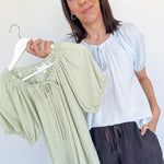 Woman holding a hanger with green striped pants against a white background