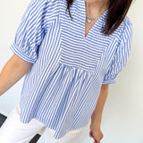Woman wearing a blue and white striped blouse with white pants against a white background