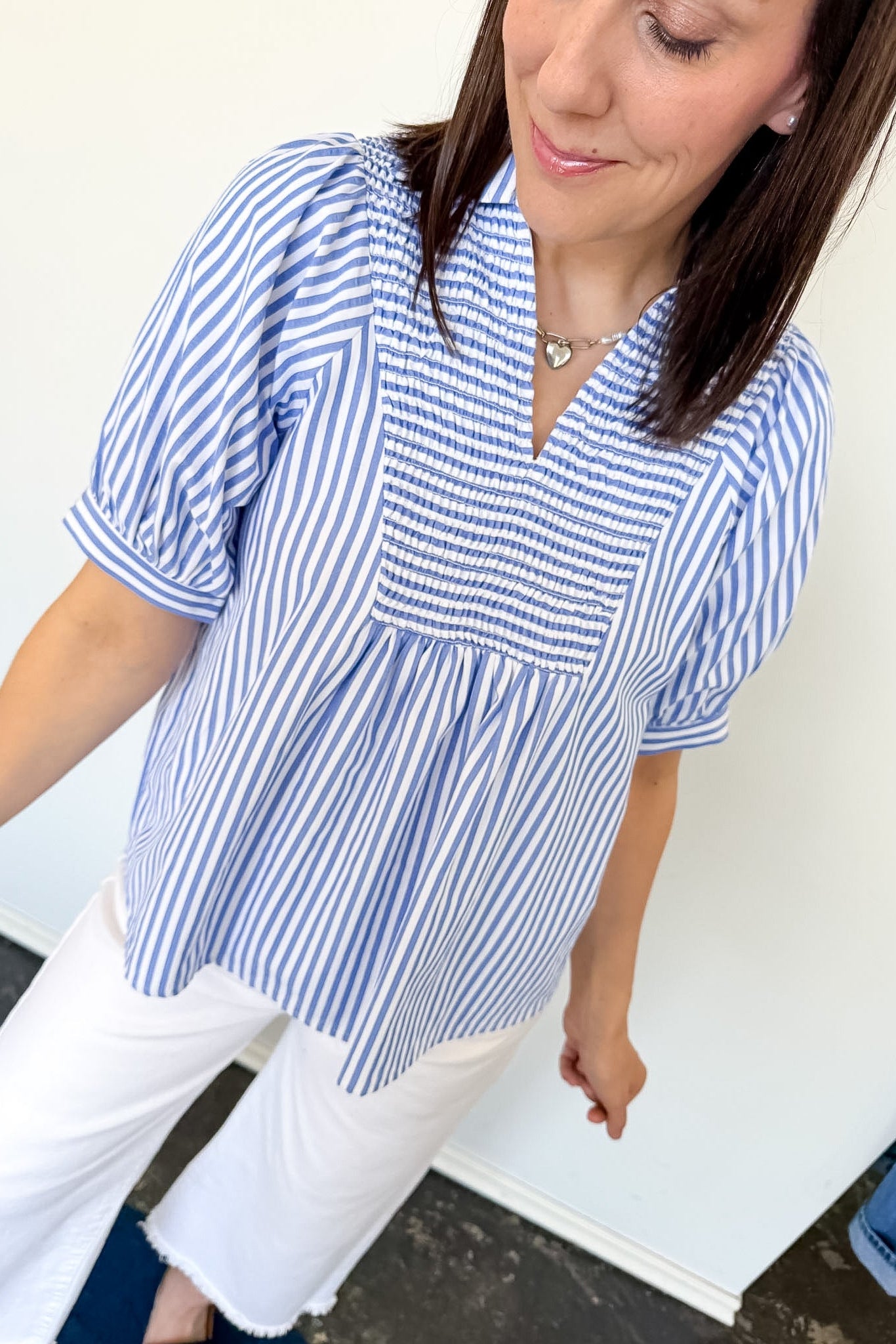 Woman wearing a blue and white striped blouse with white pants against a white background