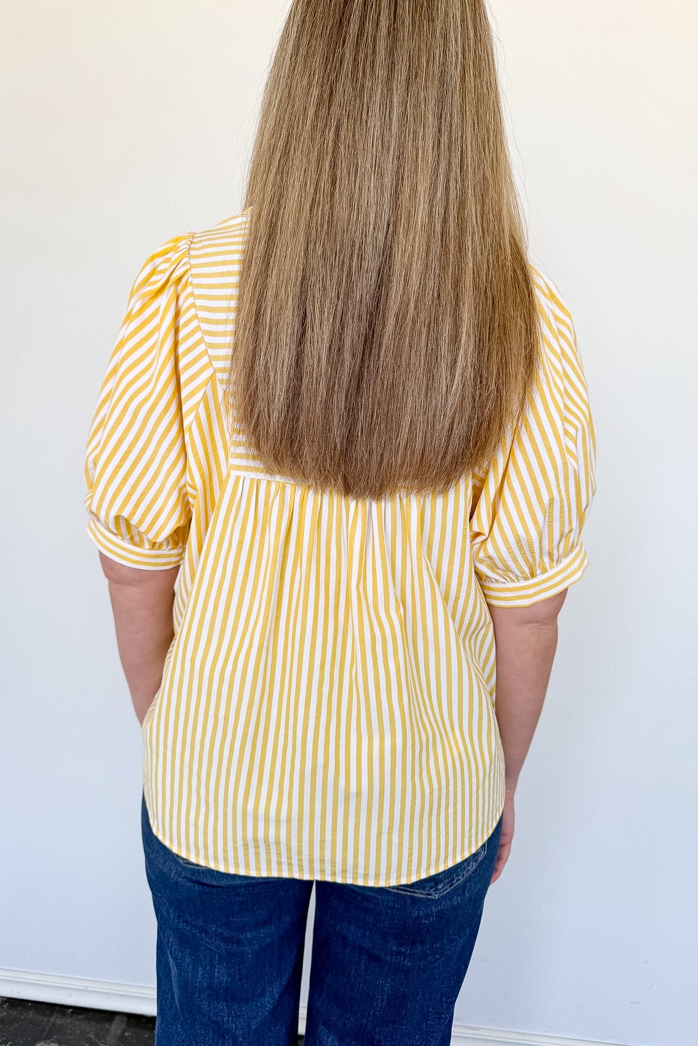 Person wearing a yellow and white striped shirt with blue jeans against a white background