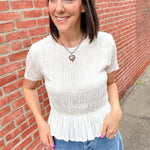 Woman wearing a white peplum top and blue jeans standing against a brick wall.